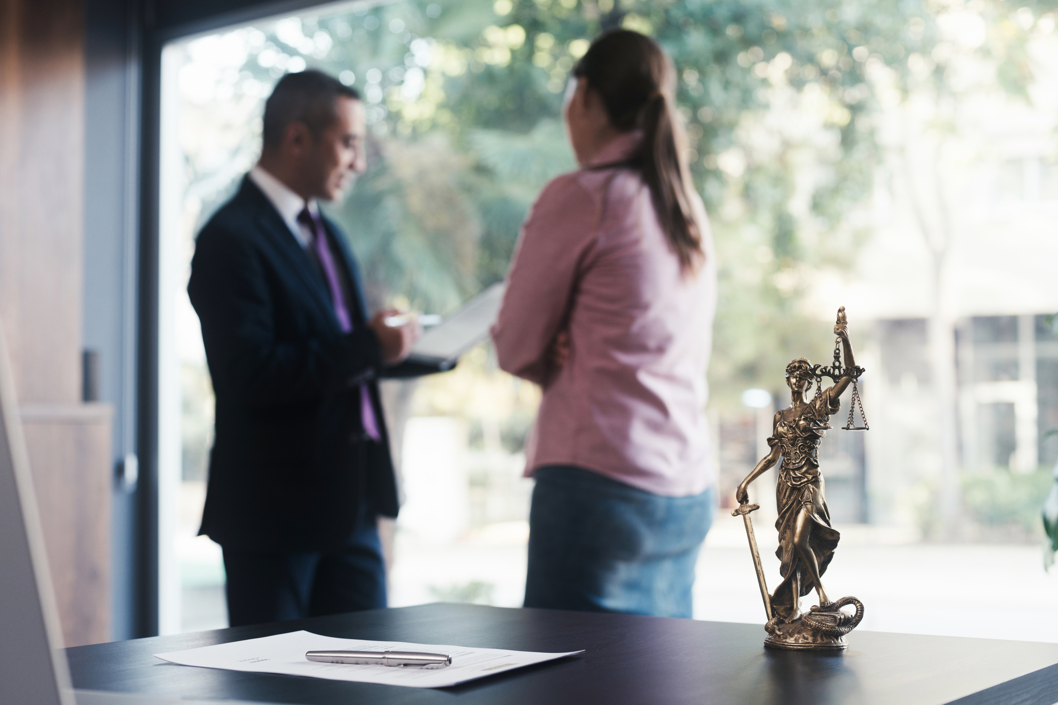Lawyer consults client, Lady Justice in foreground