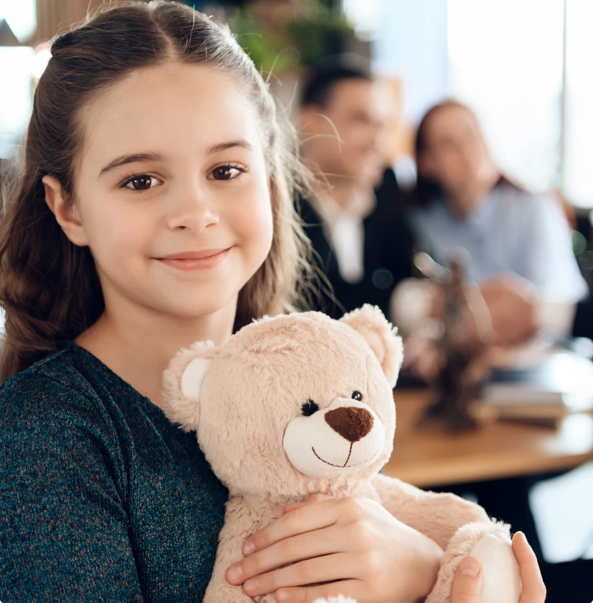 Happy child with teddy bear, family in background