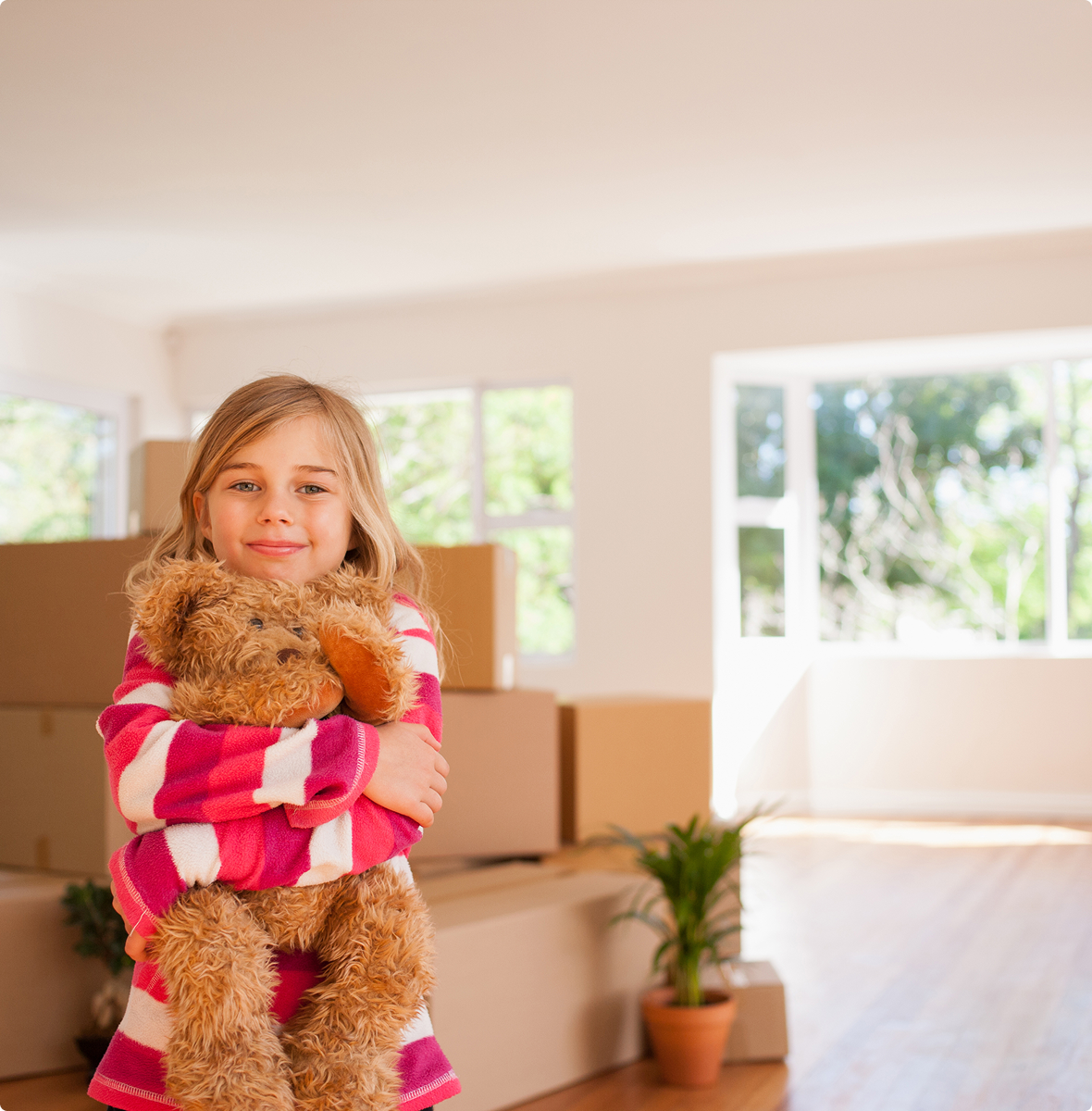 Girl holding teddy bear, moving boxes behind her